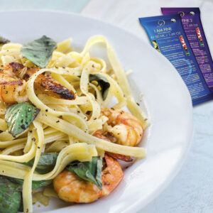 Pasta with prawns and basil leaves on white plate.